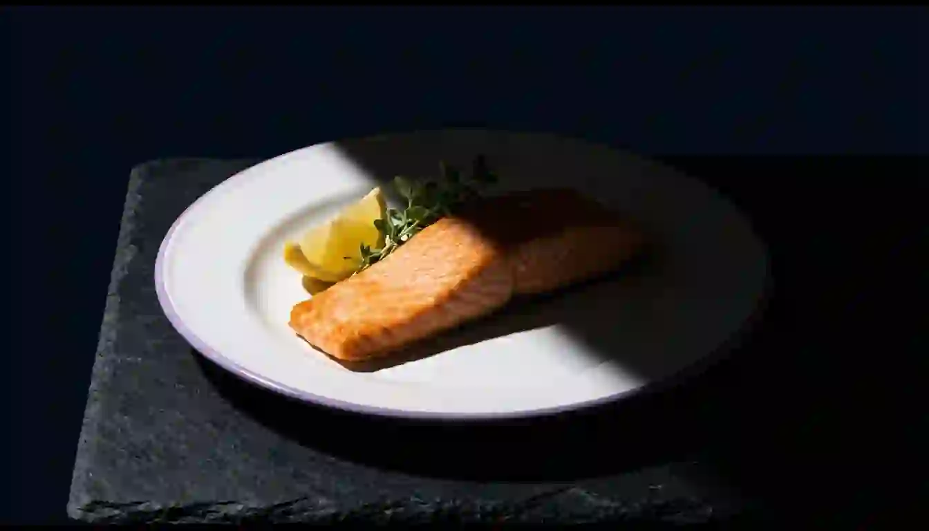 Plato con un filete de salmón partido por una diagonal de luz: media ración nítida y la otra media desaparecida en la sombra
